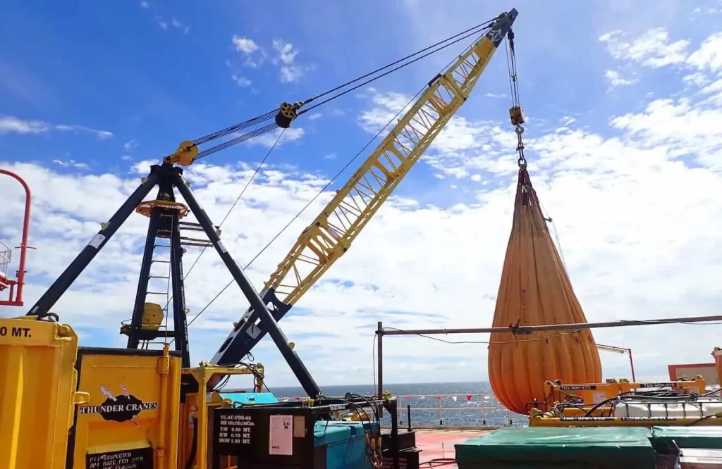 Load testing operation with Thunder Crane yellow modular equipment lifting heavy test bag on offshore rig