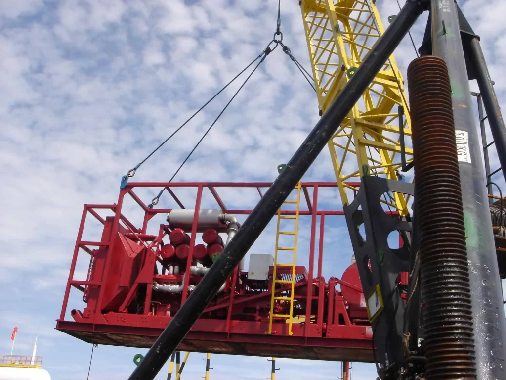Thunder Crane lifting red pumping fluid engine equipment on offshore platform with yellow crane machinery