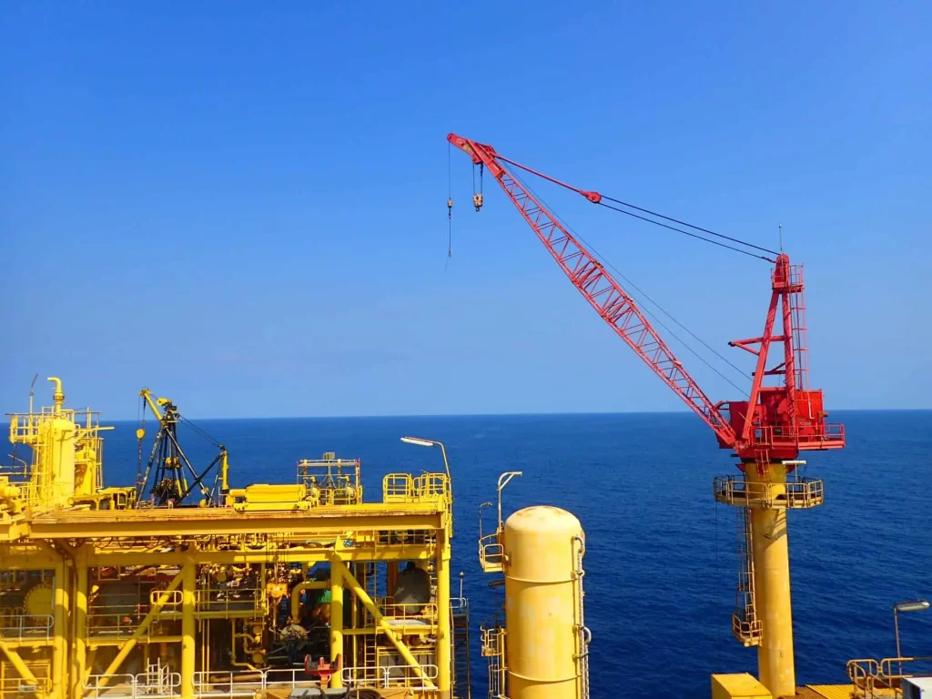 Offshore Angola platform with red industrial lifting equipment and yellow infrastructure over blue ocean waters